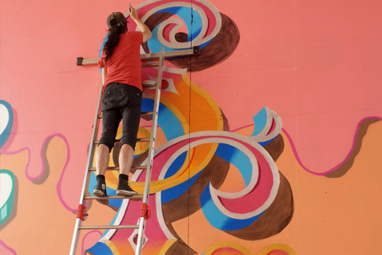 Jill Strong sur une échelle en traine de peintre une fresque